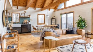 A spacious living area with a wooden ceiling, a sofa, a coffee table, and a dining table with chairs.