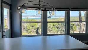 Eine Küche mit einer großen Kochinsel, drei Fenstern mit Blick auf Strand und Bäume sowie einer Pendelleuchte.