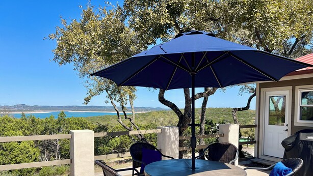 Eine Terrasse im Freien mit Tisch und Stühlen, einem blauen Sonnenschirm und Blick auf die Küste.