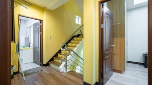 A hallway with a staircase, wooden flooring, and a door leading to a room.