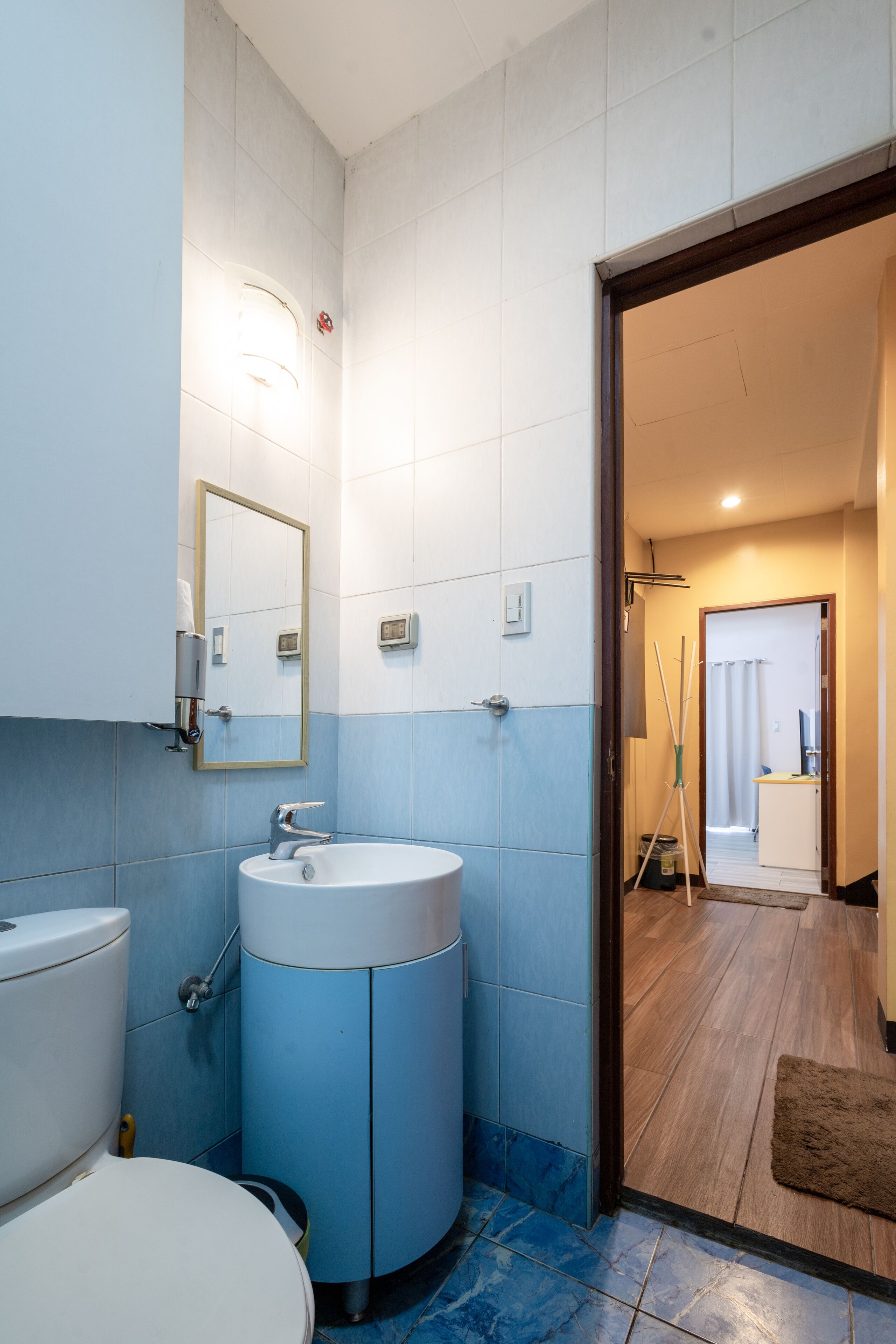 A bathroom with a toilet, sink, and mirror. There is a door leading to another room.