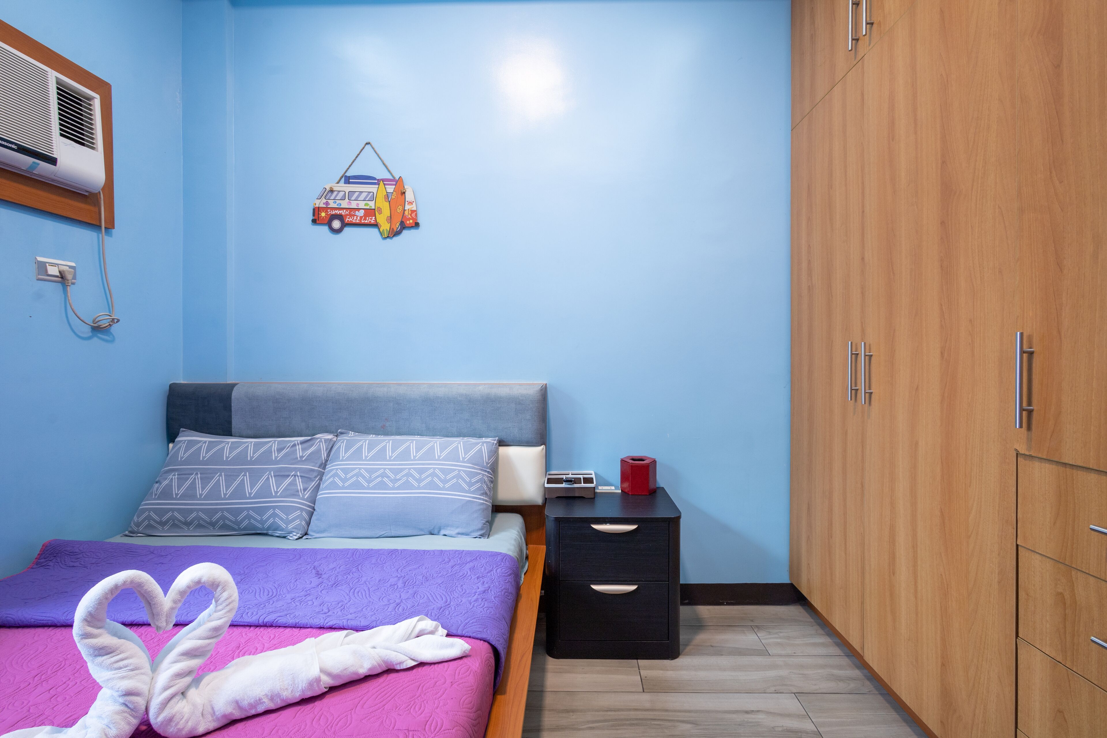 A bedroom with a bed, pillows, a bedside table, a nightstand, a wardrobe, and a wall-mounted heater.