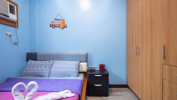 A bedroom with a bed, pillows, a bedside table, a nightstand, a wardrobe, and a wall-mounted heater.