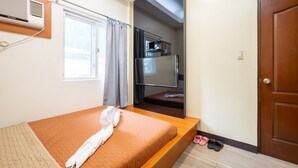 A bedroom with a bed, a window with curtains, a mirror, a wardrobe, and a door.