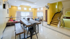 A spacious living area with a wooden dining table, chairs, a sofa, and a staircase leading to an upper floor.