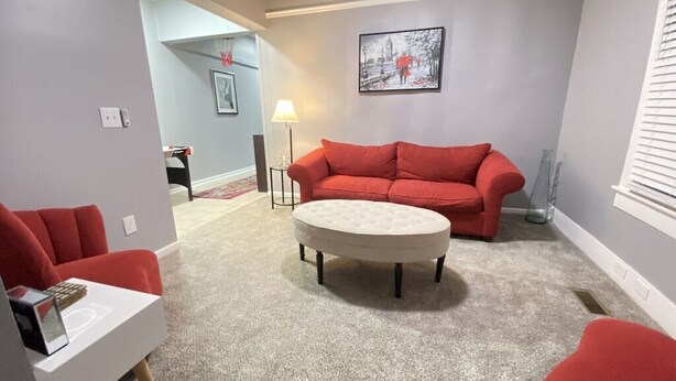 Una sala de estar con un sofá rojo, un reposapiés redondo y una mesa de centro blanca.