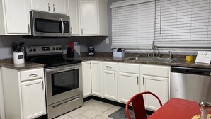 Una cocina con armarios blancos, horno de acero inoxidable, microondas, lavamanos y una mesa de comedor roja.
