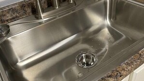Un lavamanos de acero inoxidable con un solo grifo, un desagüe y una encimera de granito.