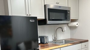A modern kitchen with white cabinets, a black refrigerator, a microwave, a toaster, and a wooden countertop. - Cozy, modern suite in the heart of Loveland Colorado. (Loveland)