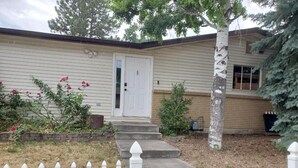 A two-story house with a front door, steps leading to the entrance, a white picket fence, and a small garden with red flowers. - Cozy, modern suite in the heart of Loveland Colorado. (Loveland)