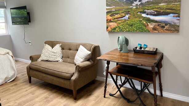 A living room with a brown sofa, a wooden table, a TV mounted on the wall, and a landscape painting. - Cozy, modern suite in the heart of Loveland Colorado. (Loveland)