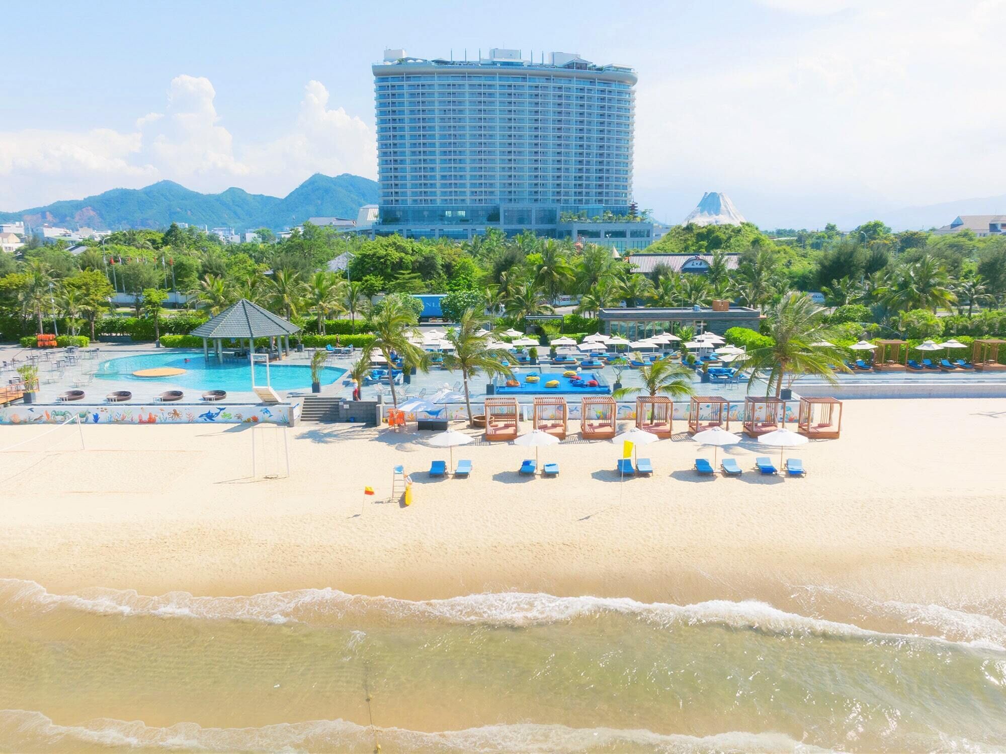 A beach resort with multiple swimming pools, palm trees, and a large hotel building in the background.