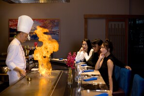 A chef performing a fire act at a restaurant with a dining table and chairs visible. - Mikazuki Villas - The Ryokan (Da Nang)