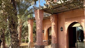 Un bâtiment avec des piliers en briques, un patio couvert et une porte donnant sur une pièce.