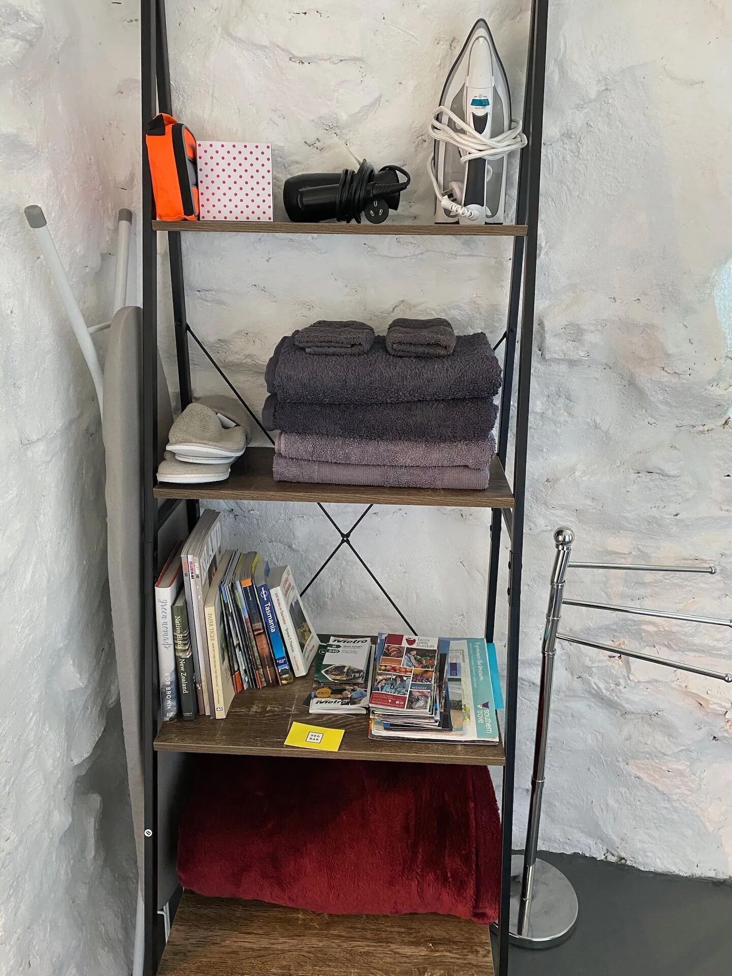 A metal shelf with folded towels, a hairdryer, and a polka-dotted bag.
