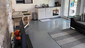 Et moderne køkken med hvide skabe, en indbygget ovn og en mikrobølgeovn. Der er et spiseområde med et bord og stole, og en sofa i opholdsstuen.