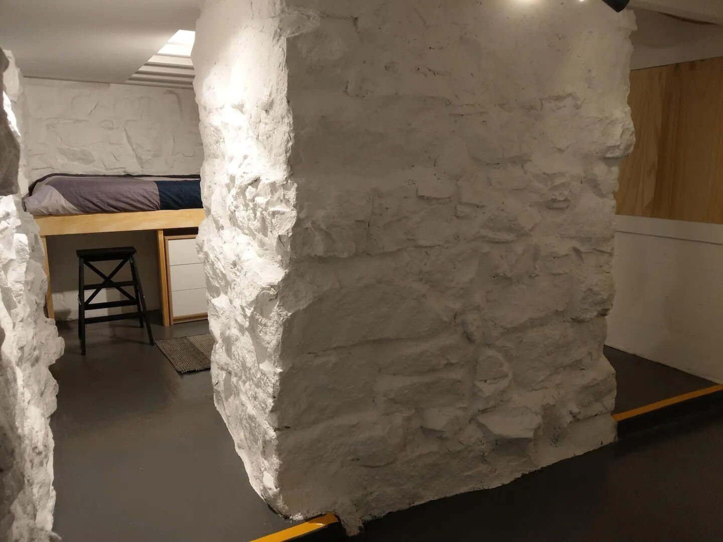 A room with a bunk bed, a small stool, and a white textured wall.