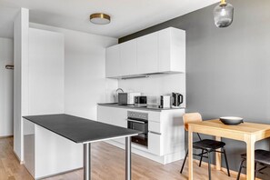 A modern kitchen with white cabinets, a black countertop, and a wooden dining table with two chairs.