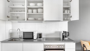 Une cuisine moderne avec des meubles blancs, un four encastré, un four à micro-ondes, une machine à café et un évier.