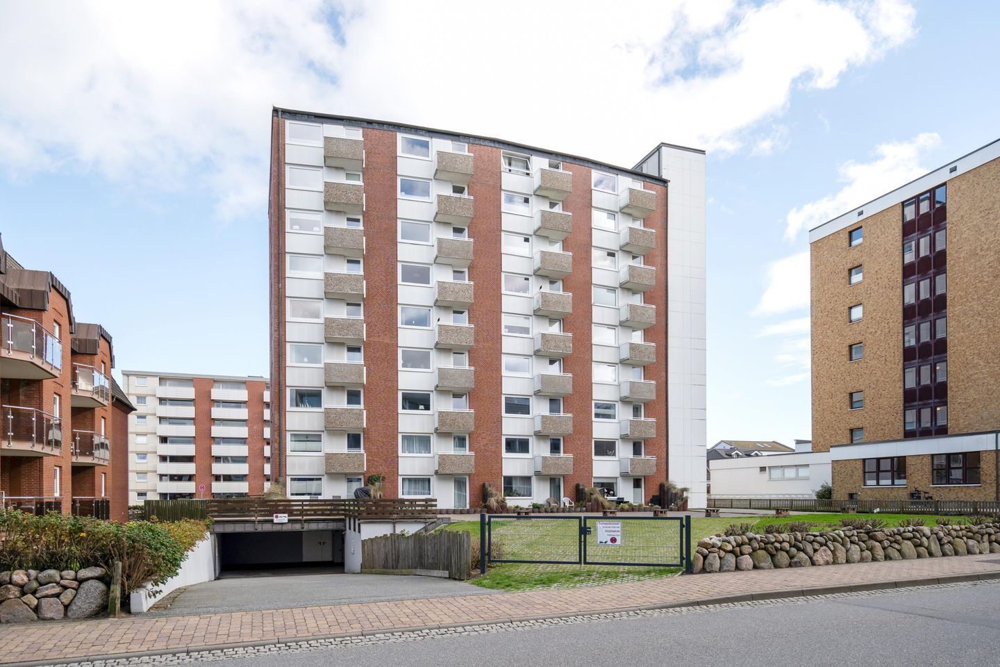 A multi-story residential building with a brick facade, balconies, and a gated entrance.