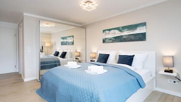 A modern hotel room with a large bed, a mirror, a painting, and a bedside table with a lamp.