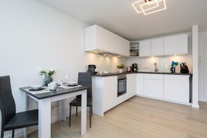 A modern kitchen with white cabinets, a dining area with a table and chairs, and a built-in oven. - Ocean View II - Modern apartment with ocean view, west-facing balcony, Wi-Fi. Pets allowed. (Sylt)