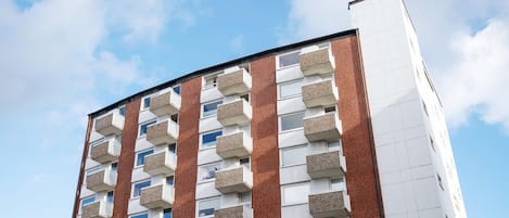Un immeuble à plusieurs étages, doté d’une façade en briques et de balcons blancs.