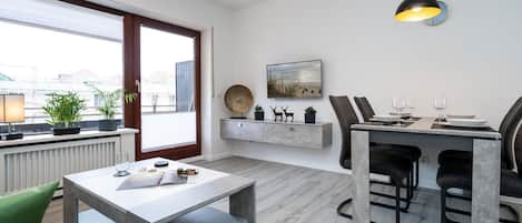 A modern living room with a dining area, a large window, and a view of the city.