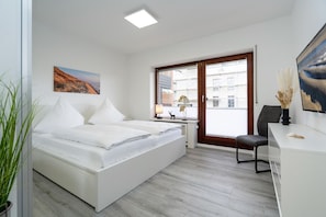 Moderni hotellihuone, jossa on suuri sänky, työpöytä ja suuri ikkuna, josta avautuu näkymä kaupunkiin.
