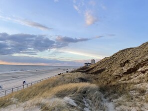 A beach with a sandy shore, a grassy dune, and a building in the background.
