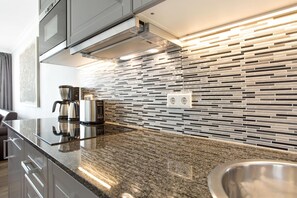A modern kitchen with a granite countertop, stainless steel appliances, and a backsplash with horizontal tiles. - SyltMomente - 2-room apartment close to the beach: balcony, parking space, WLAN. Pets (Sylt)