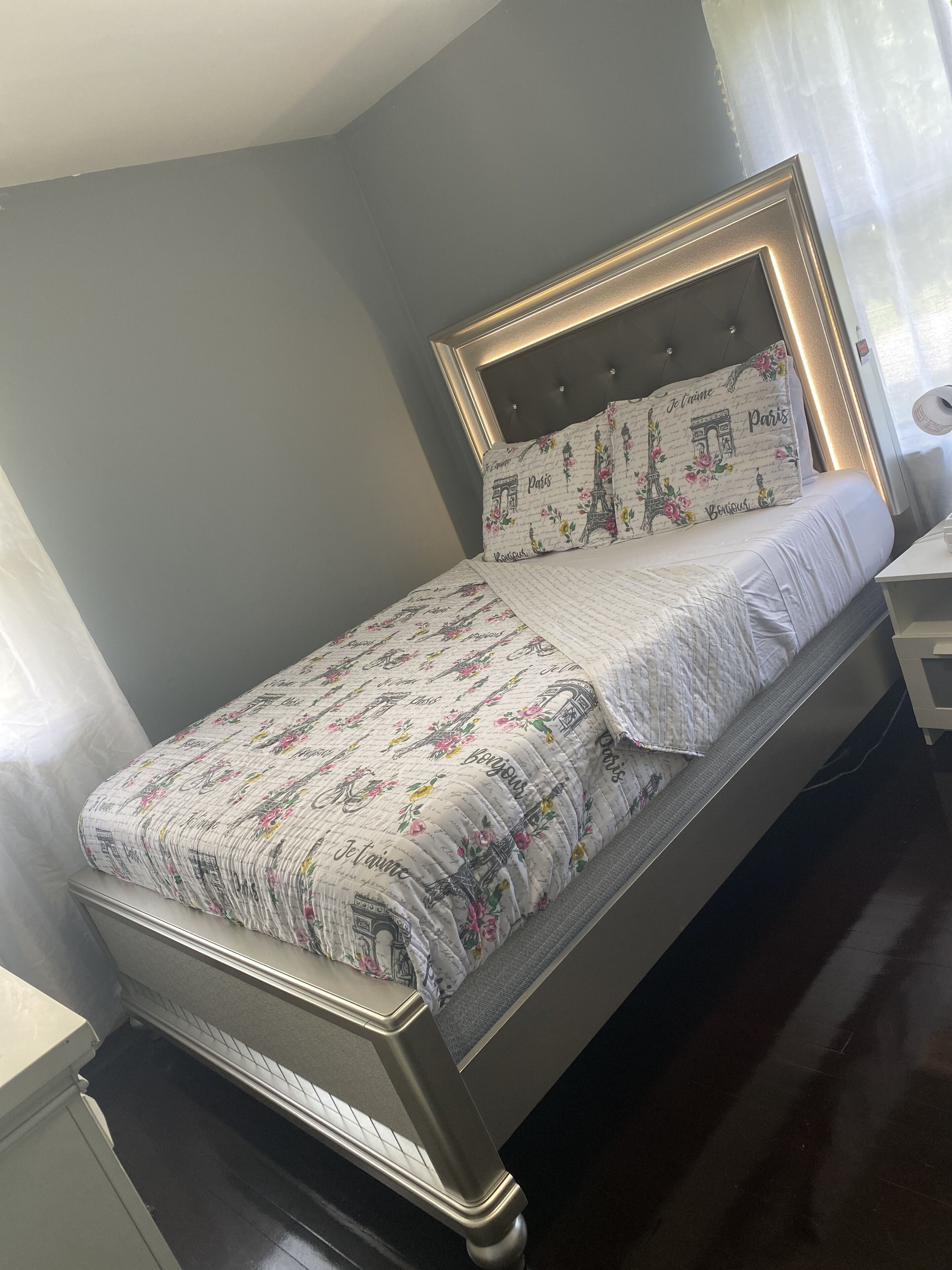 Una cama bien hecha con una colcha estampada de flores y almohadas a juego, un cabecero de madera y una mesita de noche con una lámpara.