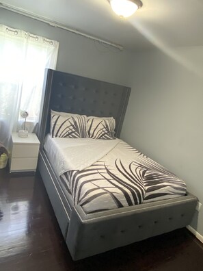Un dormitorio con cama, mesita de noche y ventana con cortinas.