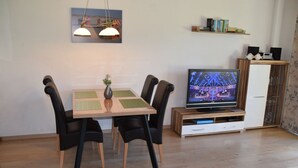 Un comedor con una mesa, sillas, un florero y un televisor sobre un soporte de madera.