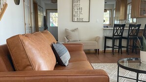 A modern living room with a leather sofa, a glass coffee table, and a kitchen in the background. - Maple Haven :: Modern, year round home on Maple Lake in Mentor, MN (Mentor)