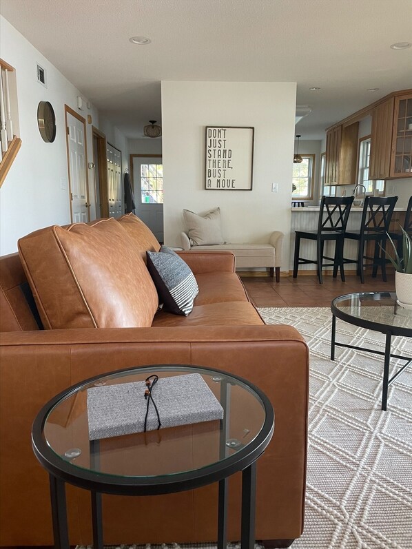 A modern living room with a leather sofa, a glass coffee table, and a kitchen in the background. - Maple Haven :: Modern, year round home on Maple Lake in Mentor, MN (Mentor)