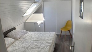 Ein kleines, modernes Schlafzimmer mit schrägem Dach, einem Bett, einem Sessel und einem Kleiderschrank.