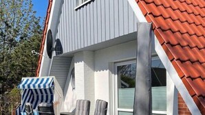 Una casa moderna con techo de tejas rojas, fachada gris y un patio con mobiliario exterior.