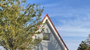 Un edificio de una sola planta con fachada blanca y tejado rojo, rodeado de follaje cuidado y un cielo despejado.