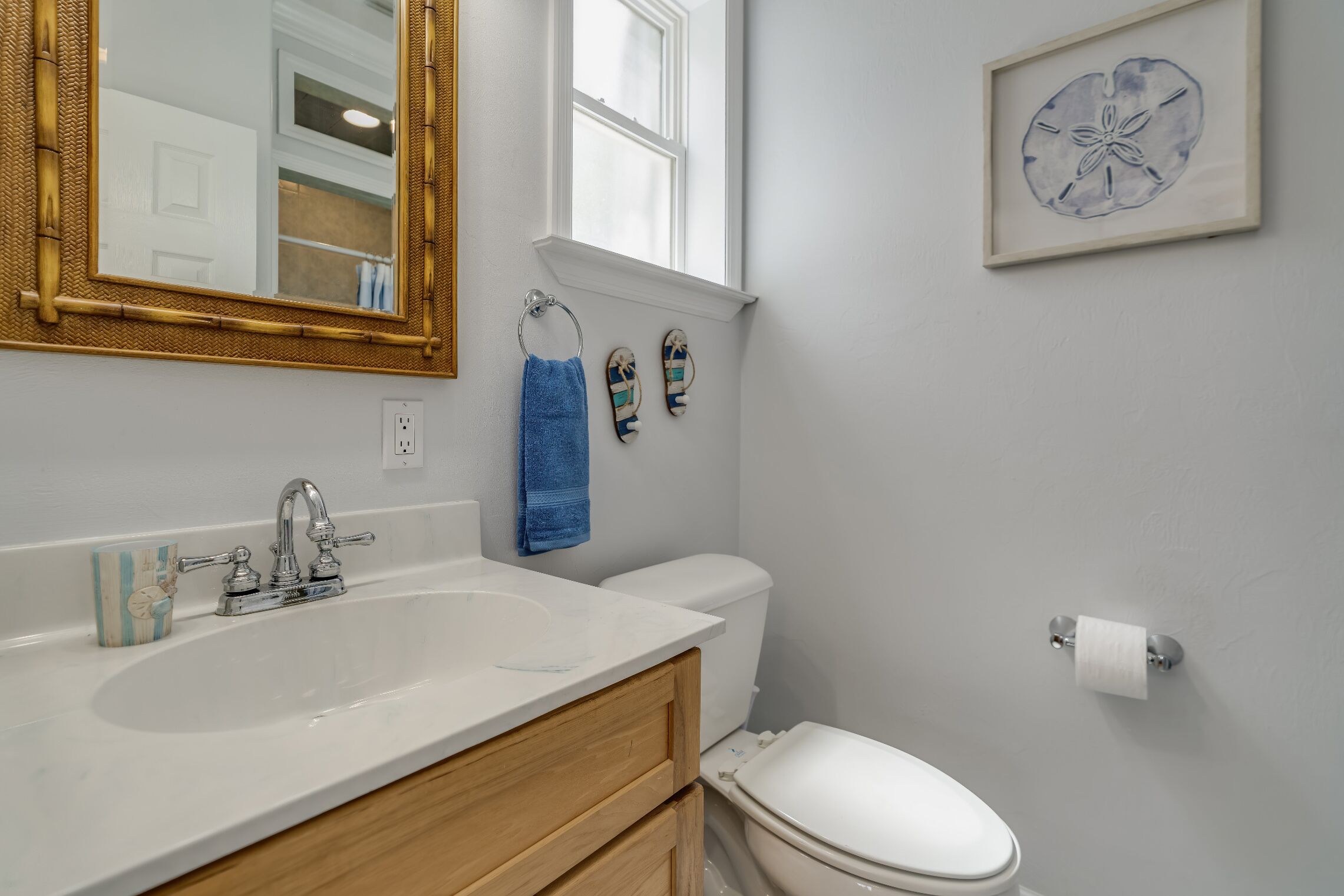 A bathroom with a white sink, a mirror with a gold frame, a toilet, and a framed picture on the wall.