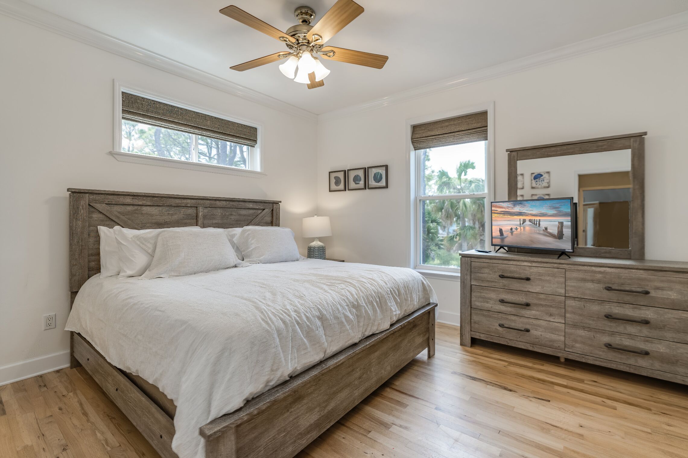 A bedroom with a wooden bed, a ceiling fan, a dresser, and a TV on a stand.