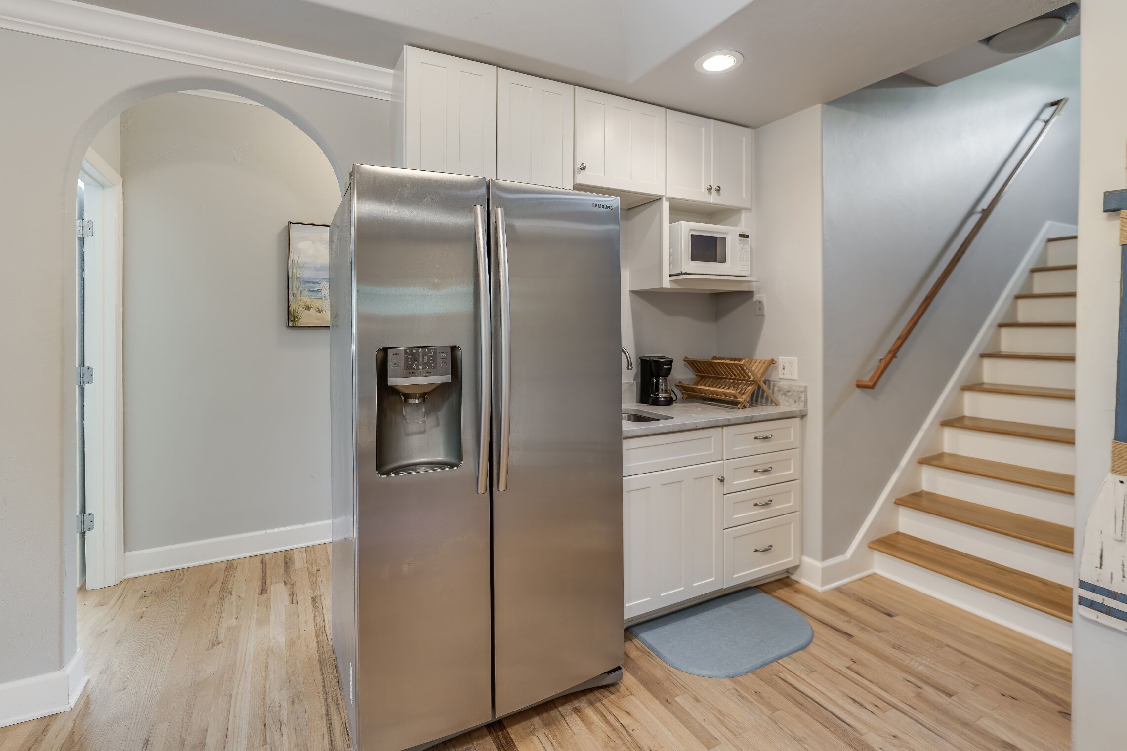 A modern kitchen with a stainless steel refrigerator, white cabinets, a microwave, and a wooden staircase.
