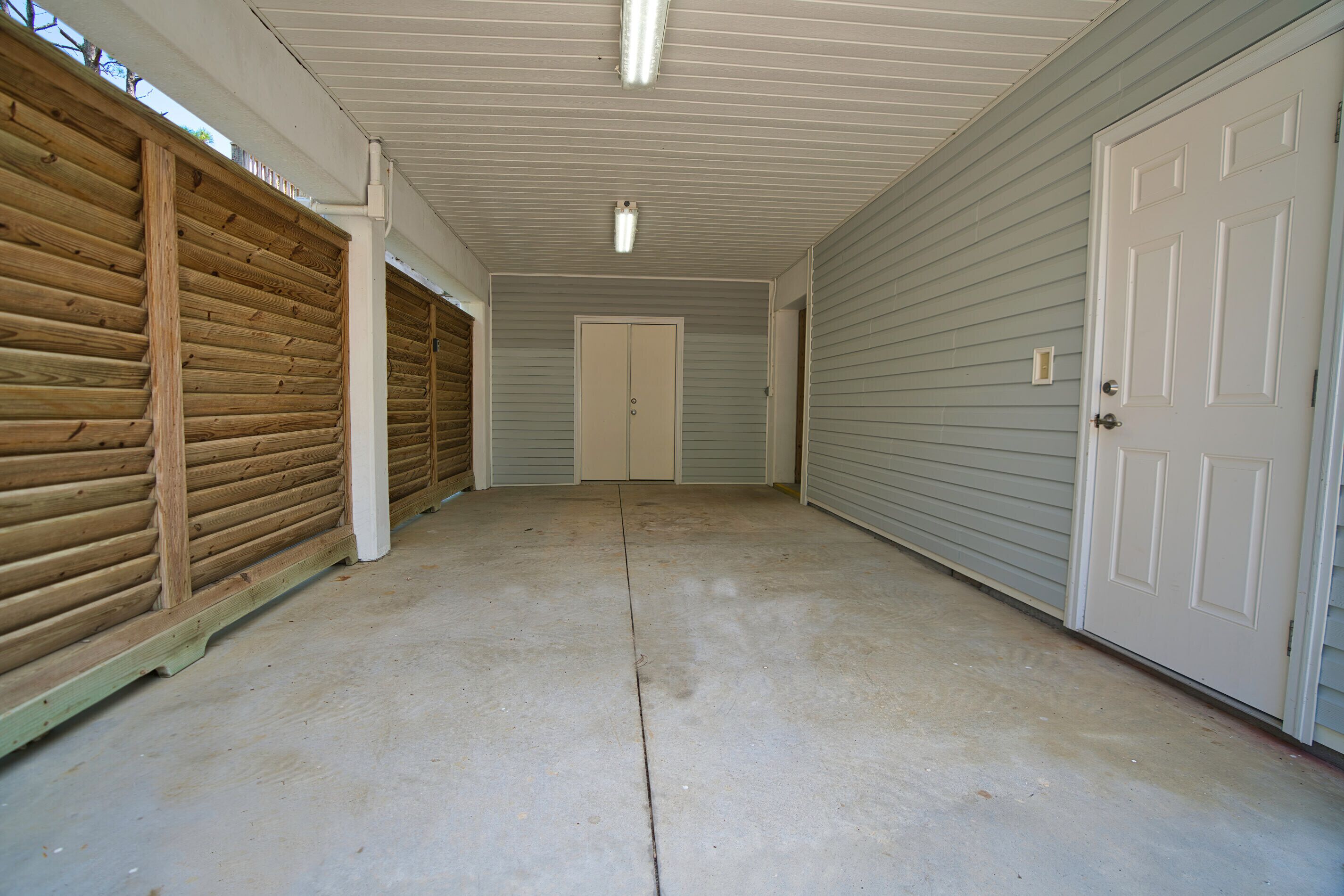 Eine Garage mit Überdachung, Betonboden, Holzwänden und einer weißen Tür.