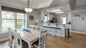 Une cuisine spacieuse avec des meubles blancs, un îlot central et un coin repas comprenant une table en bois et des chaises blanches.