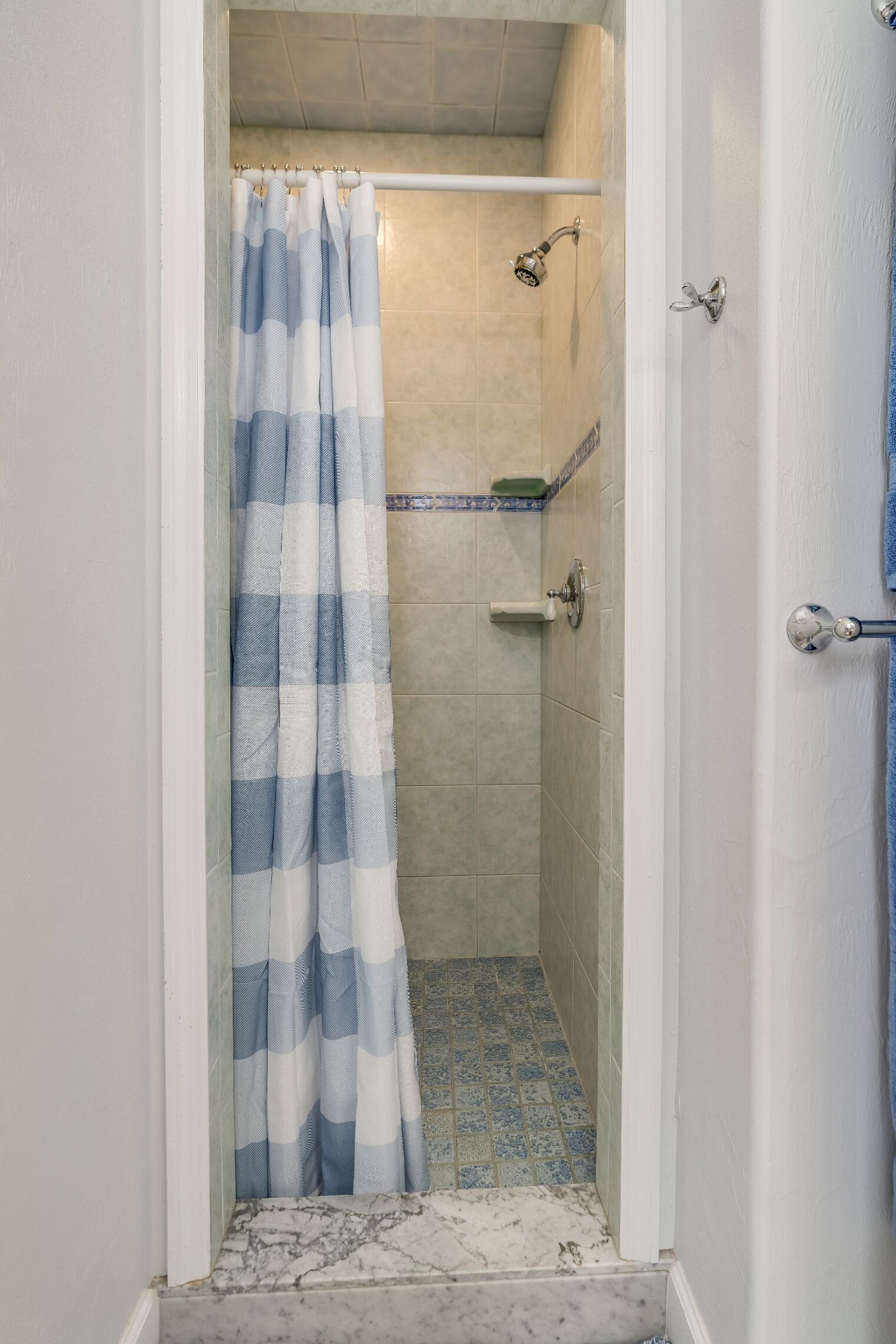 A bathroom with a shower area, a tiled floor, and a white door.