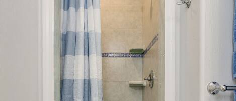 A bathroom with a shower area, a tiled floor, and a white door.