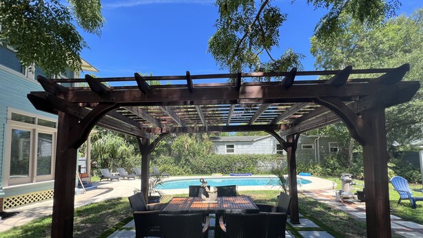 En overdækket terrasse med pool, udendørs møbler og et pergola-tag.