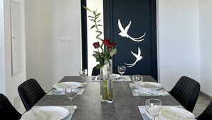 Een moderne eetkamer met een lange tafel voor zes personen, met een vaas met rode rozen, een decoratieve wand met witte vogels en een minimalistisch ontwerp.