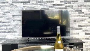 Een moderne woonkamer met een stenen muur, een flatscreen televisie, een wijnfles, twee glazen en een roos op een glazen bijzettafel.