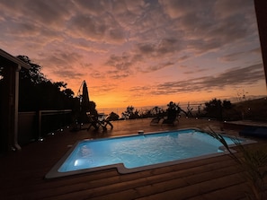 Une piscine avec une terrasse en bois, des chaises longues et une vue imprenable sur le coucher de soleil.